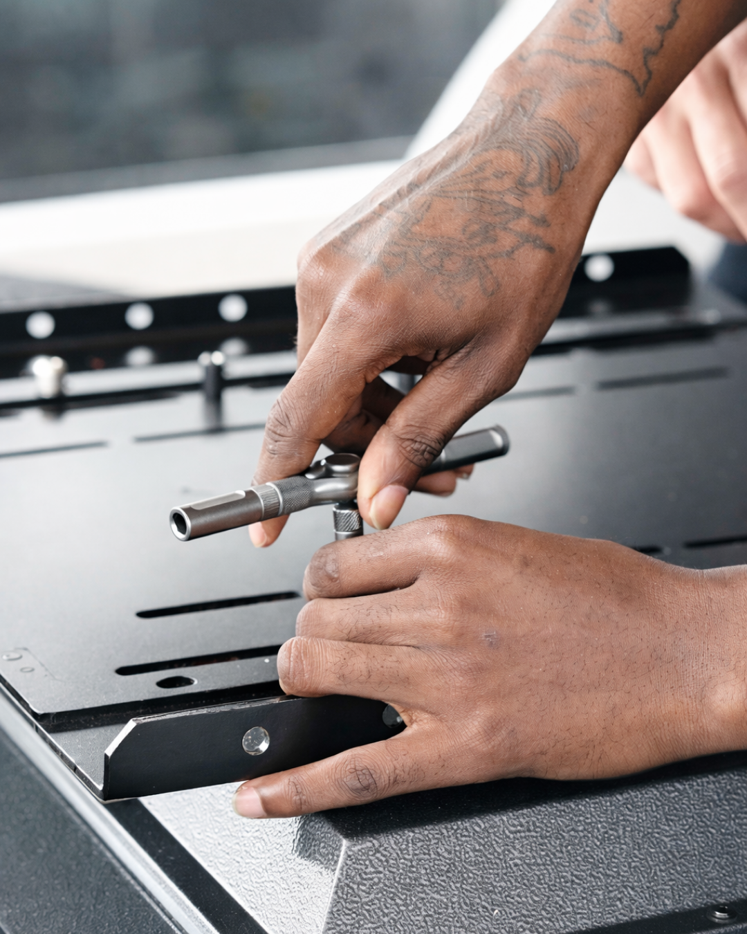 Close-up of a person using a hand tool to tighten a bolt on a black metal bracket assembly.