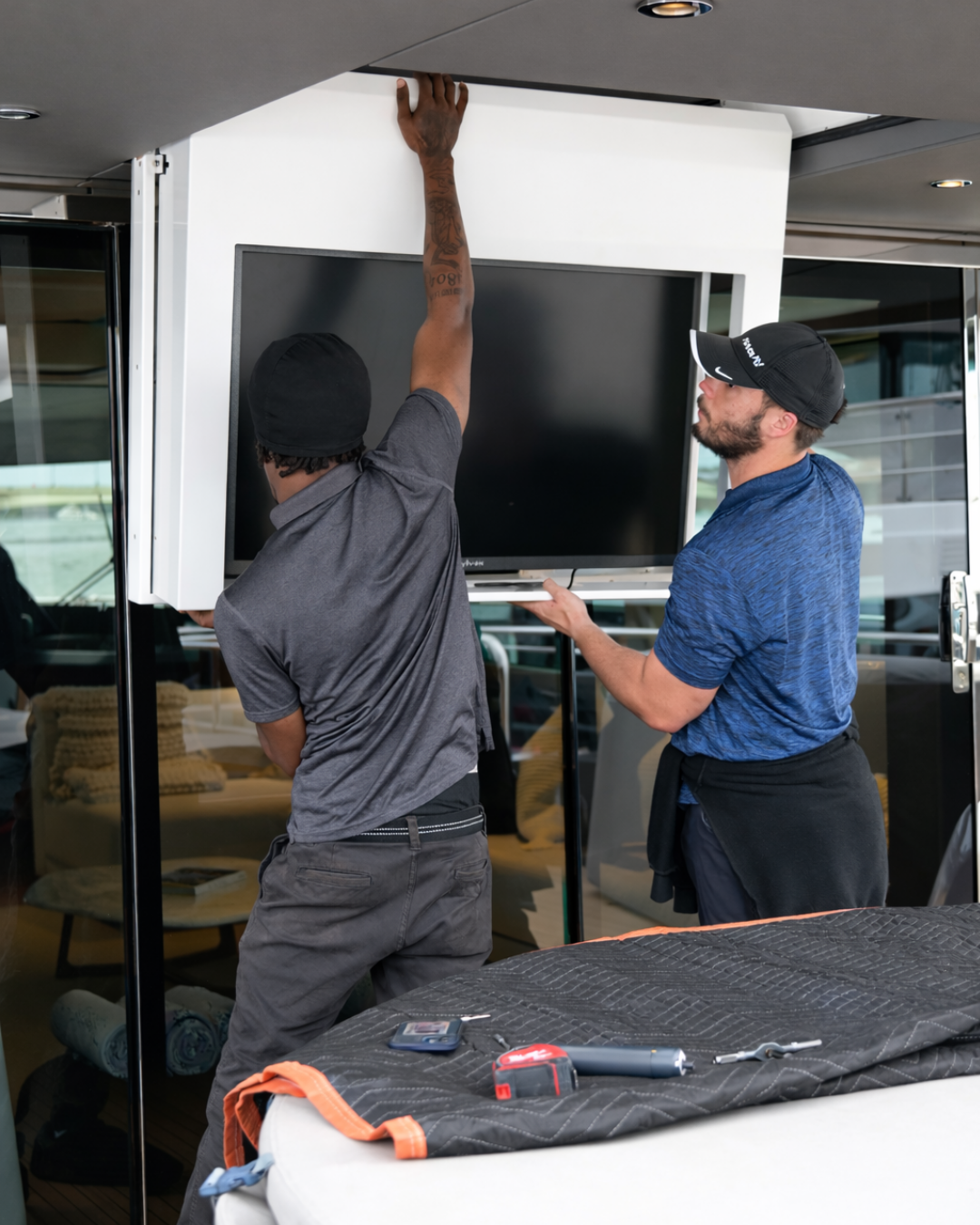Two technicians adjusting a TV display mounted inside a ceiling dropdown lift system.