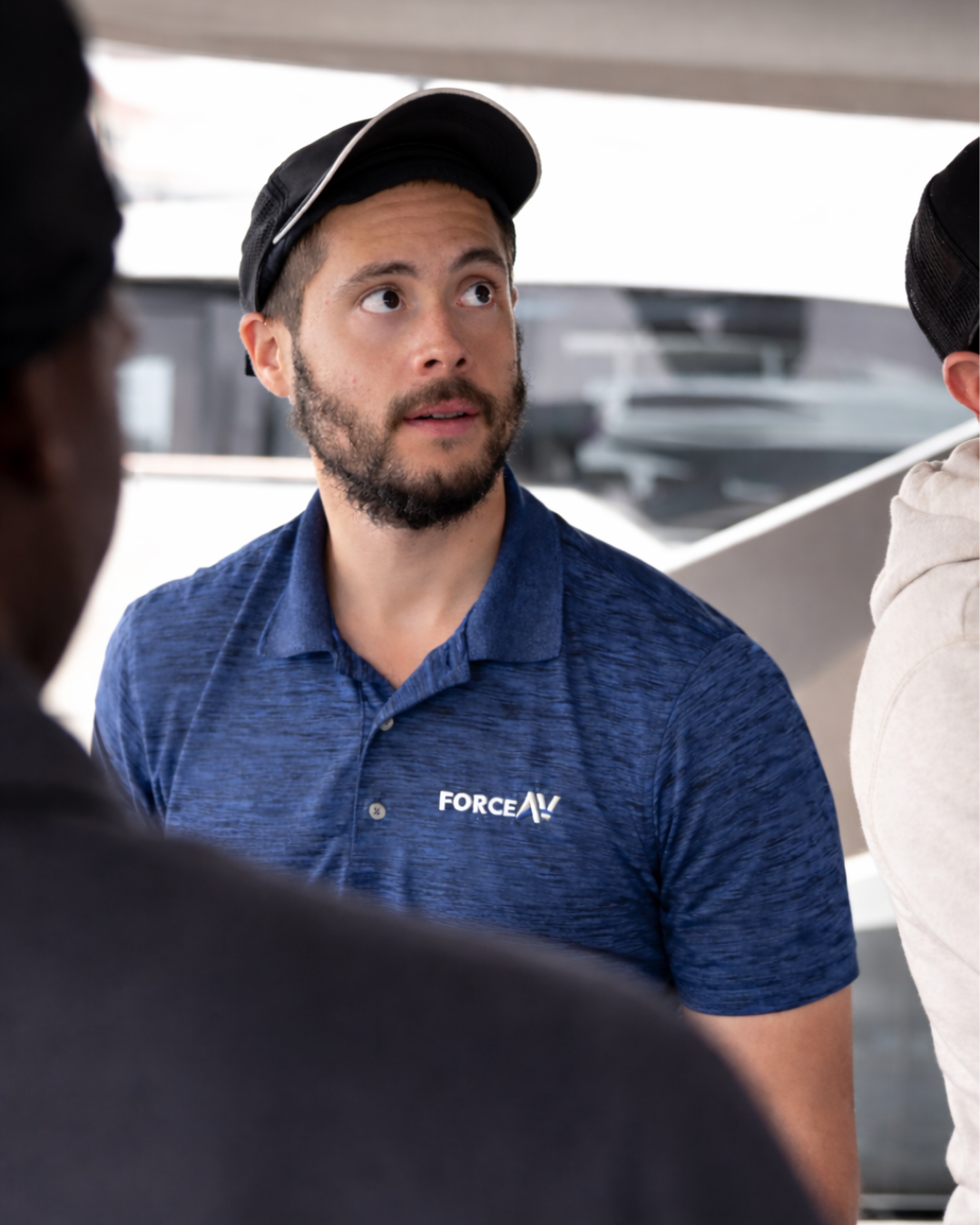 A technician in a blue Force AV polo shirt and cap looking up attentively during an installation project.