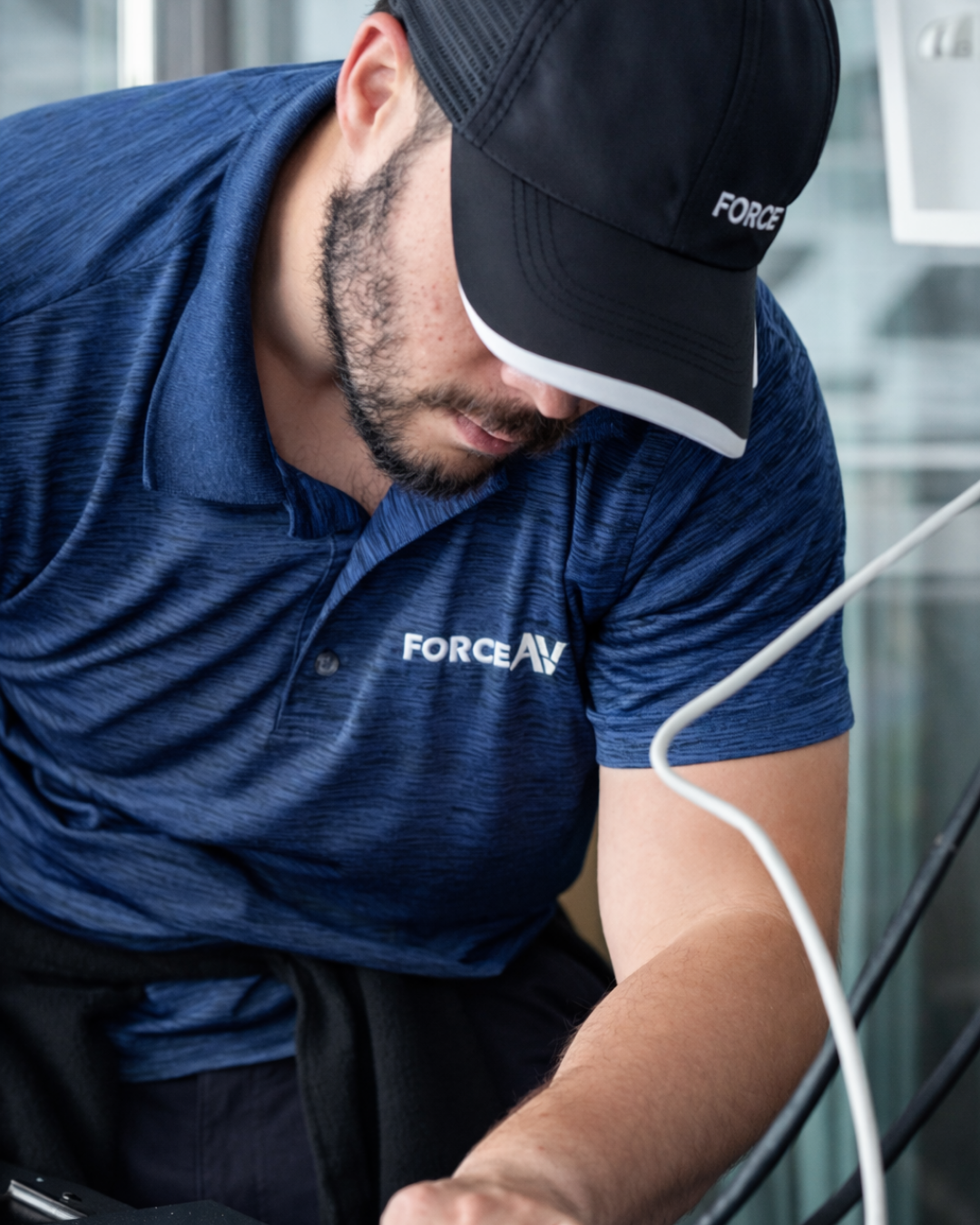 Close-up of a technician wearing a blue Force AV shirt and cap focusing on wiring work.
