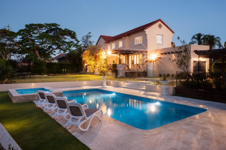 The pool and landscape of a Spanish-style home illuminated at sunset. 